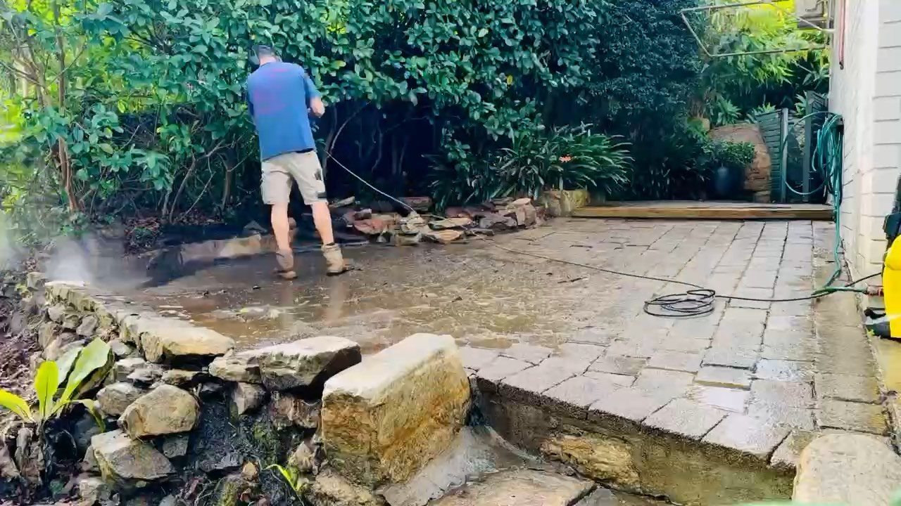 Pressure washing mossy pavers in a garden courtyard